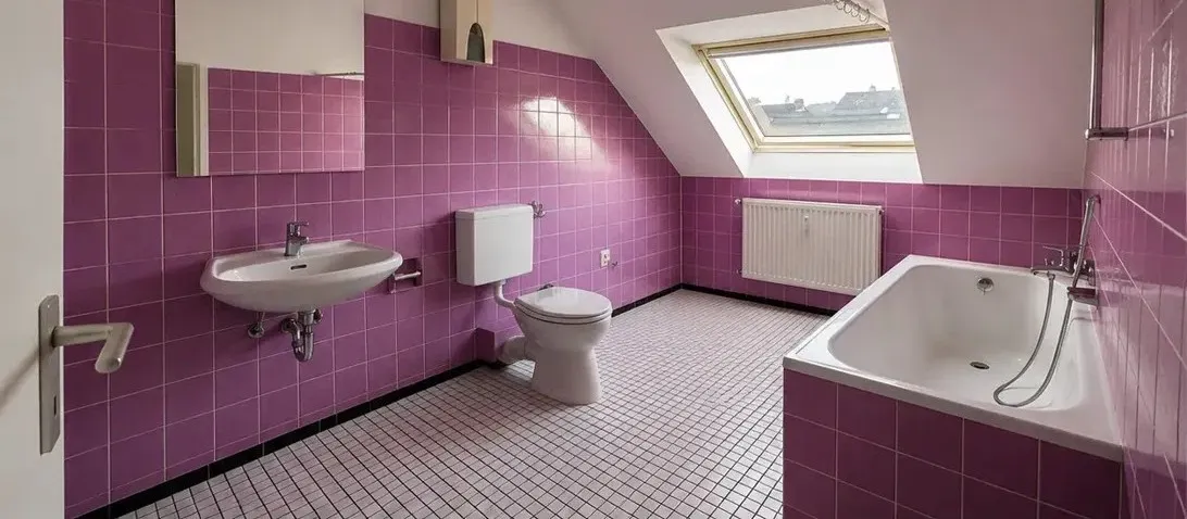 Dachgeschossbad vor der Sanierung mit lilafarbenen Wandfliesen und gemustertem Mosaikboden