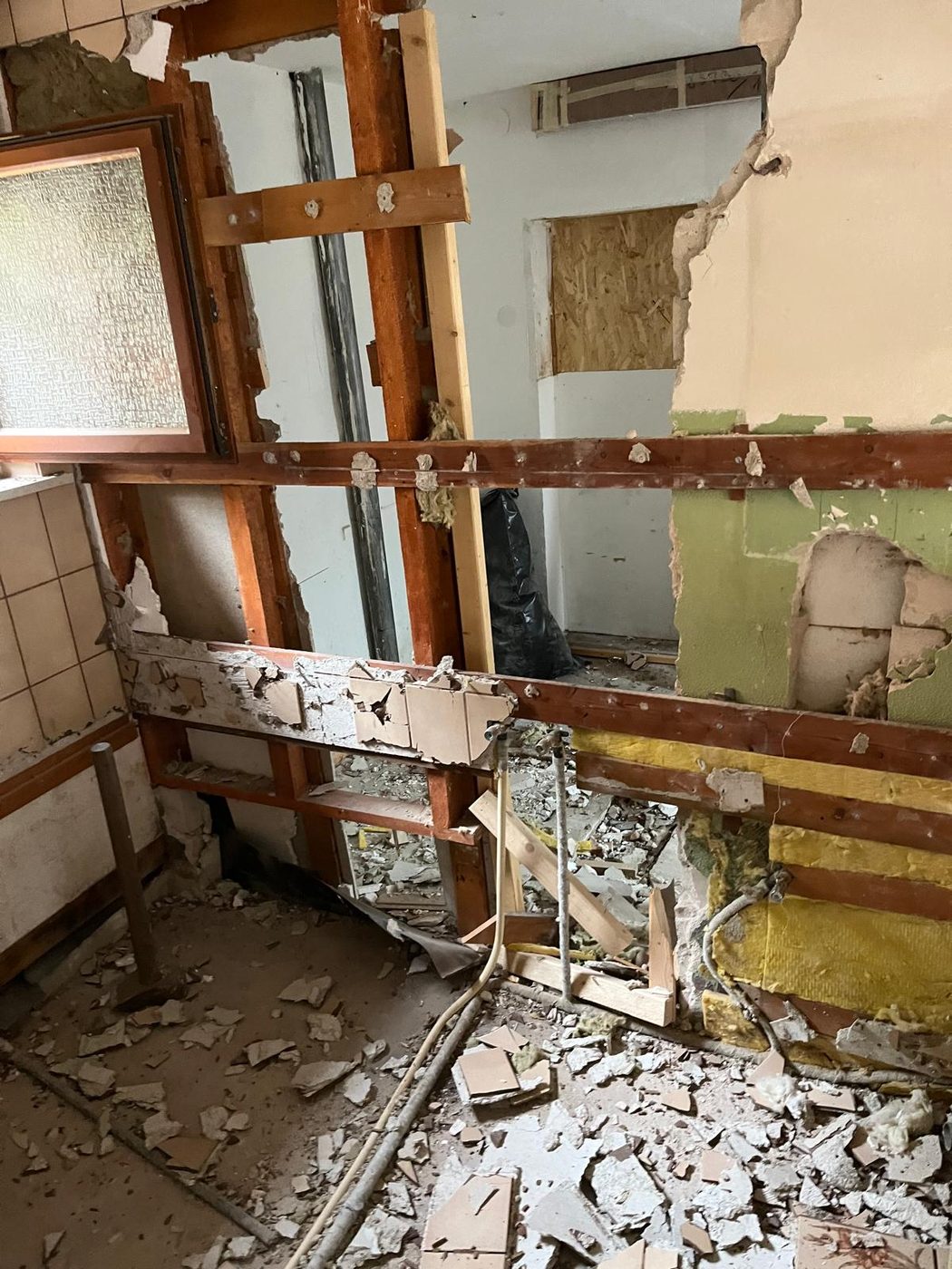 Rückbau: geöffnete Ständerwand mit freigelegten Holzstielen, Dämmung und Leitungen, Bauschutt auf dem Boden
