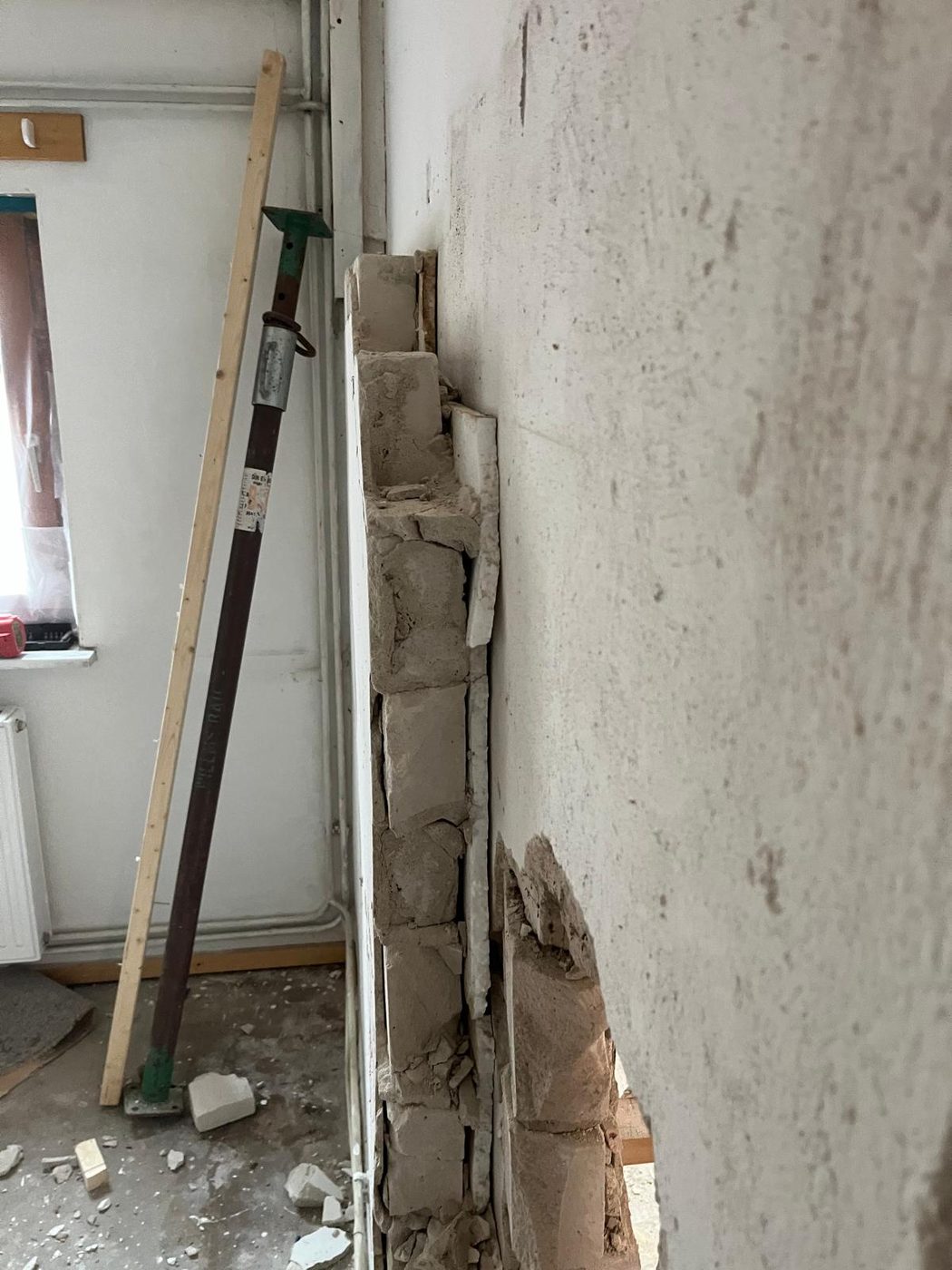Rückbau: entfernte Wandscheibe neben Betonwand, Baustütze und Werkzeug im Raum