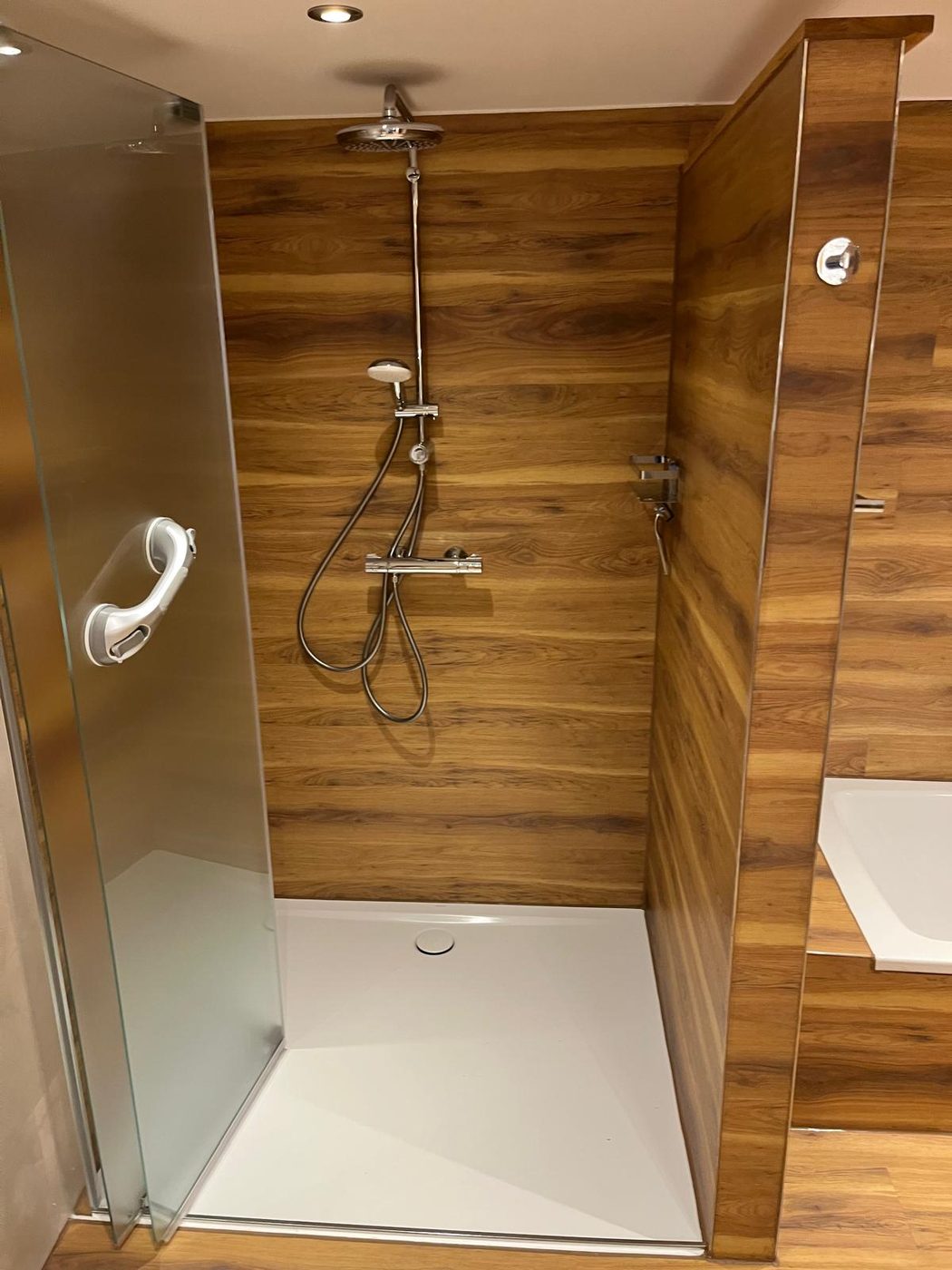 Bodengleiche Dusche mit Regendusche, Wände in Vinyl-Holzoptik, Glastür und flache weiße Duschwanne