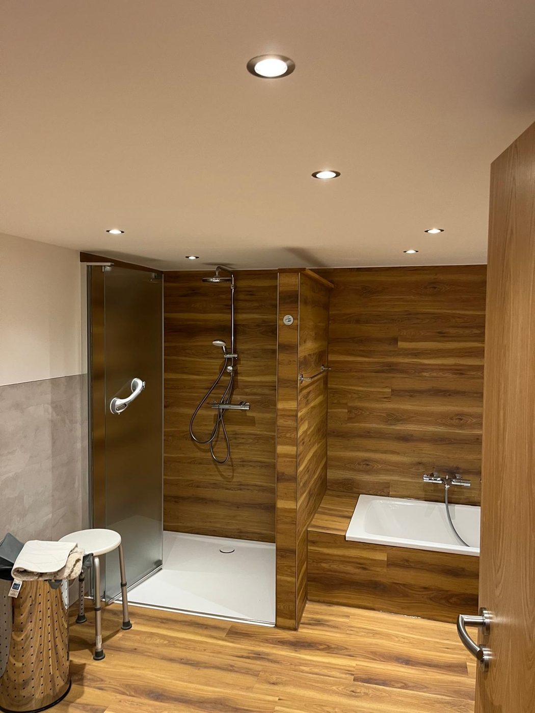 Fertiges Bad mit bodengleicher Dusche, Badewanne und Vinyl-Holzoptik an Wand und Boden
