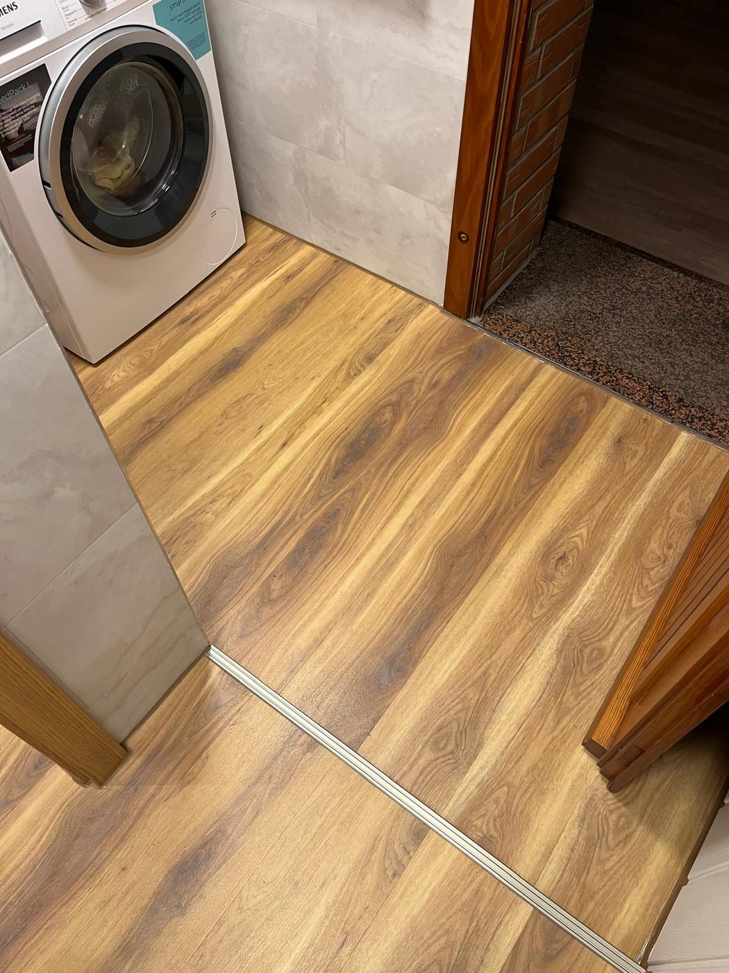 Hauswirtschaftsbereich mit Waschmaschine, Vinylboden in Holzoptik und grauen Wandfliesen