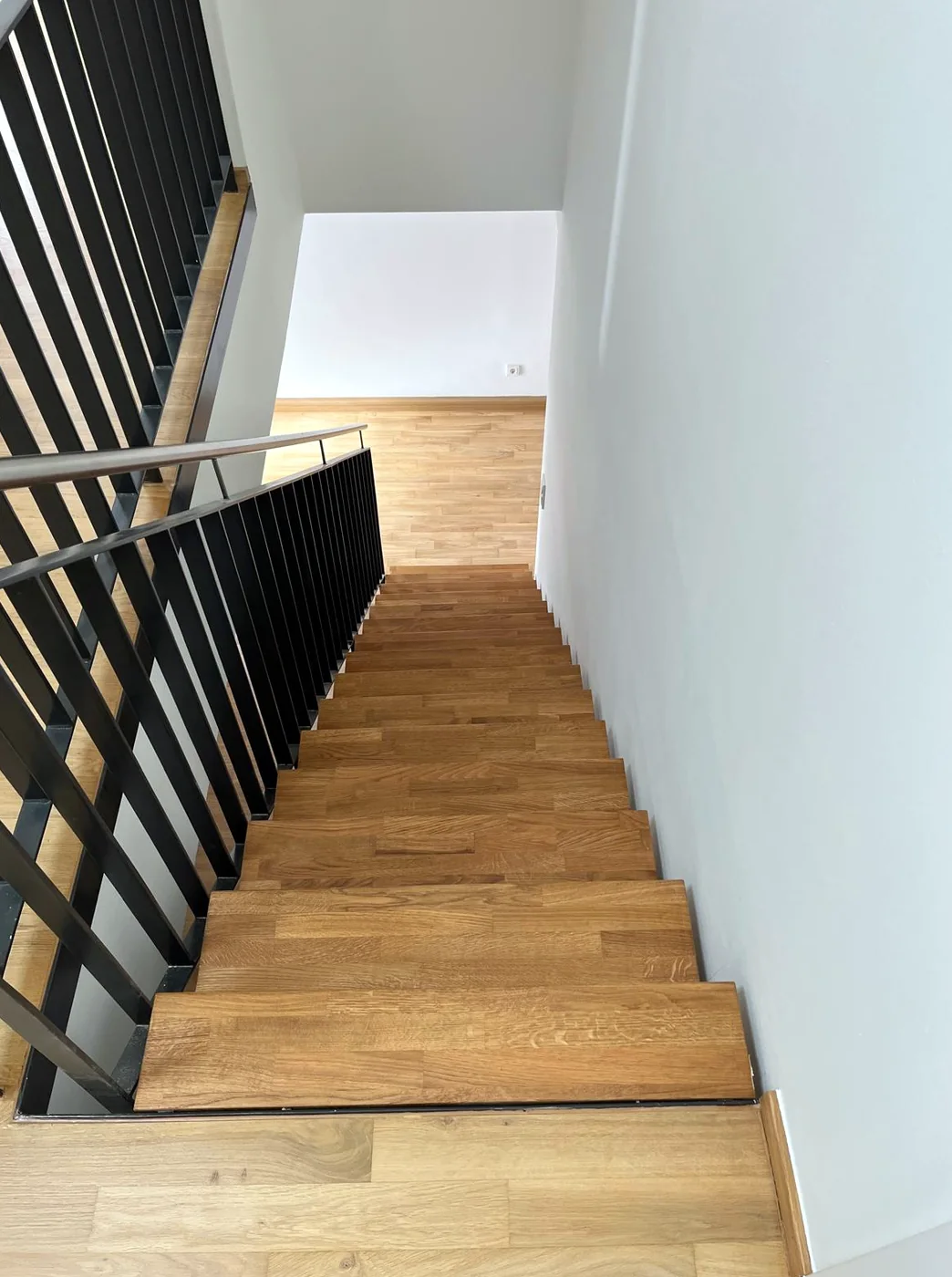 Blick von oben auf die Treppe mit versiegelten Eichenstufen und schwarzem Stahlgeländer, im Anschluss das Parkett der oberen Etage